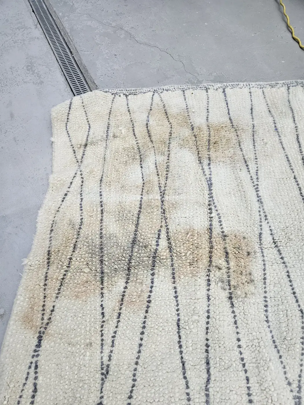Stained cream Beni Ourain rug photographed at intake before washing